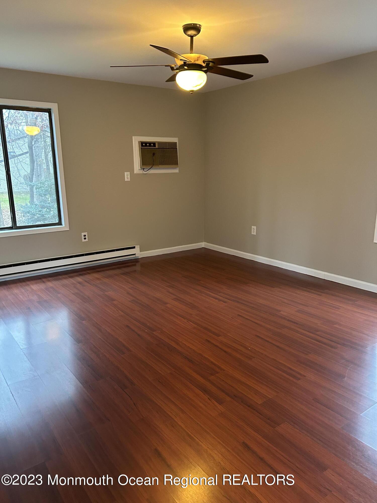 136 Amberly Drive, Unit F Manalapan, NJ 07726 - Photo 4 of 14 a view of an empty room with wooden floor ceiling fan and window