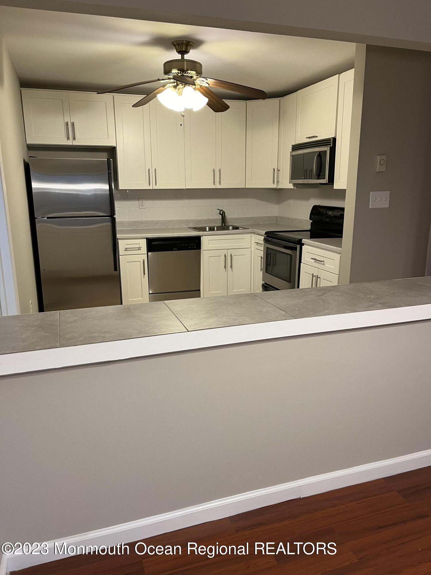 136 Amberly Drive, Unit F Manalapan, NJ 07726 - Photo 7 of 14 a kitchen with stainless steel appliances a microwave a stove and white cabinets
