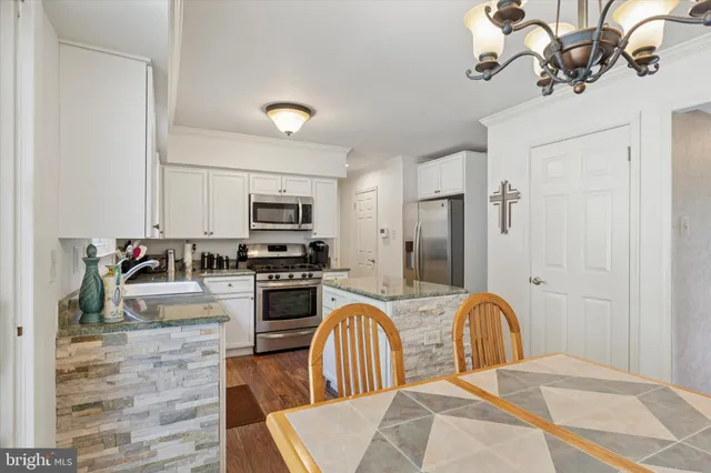 a kitchen with stainless steel appliances granite countertop a refrigerator a stove top oven a sink dishwasher and white cabinets with wooden floor