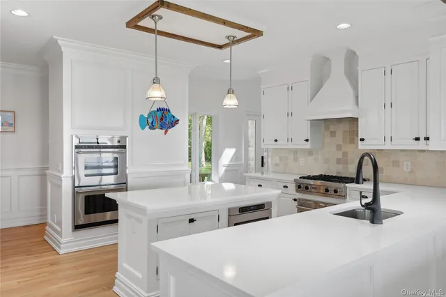 a kitchen with stainless steel appliances a stove a sink a refrigerator a center island a stove and white cabinets with wooden floor