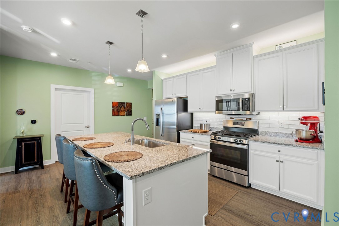 a kitchen with stainless steel appliances kitchen island granite countertop a stove a sink a refrigerator and white cabinets with wooden floor