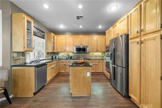 a kitchen with stainless steel appliances granite countertop a refrigerator a sink dishwasher a stove top oven a large island with wooden floor and cabinets
