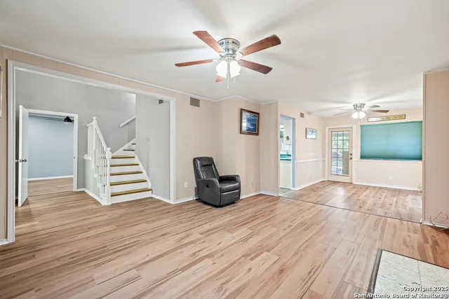 a view of an empty room with wooden floor and a ceiling fan