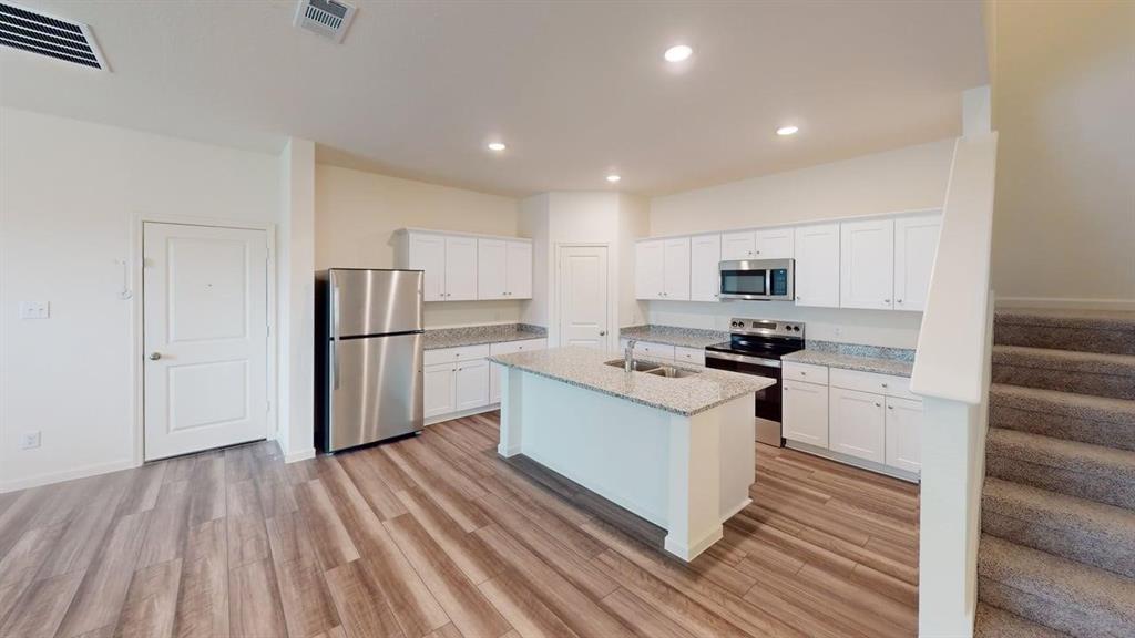 4529 Winecup Road Melissa, TX 75454 - Photo 4 of 29 Open-concept kitchen featuring white cabinetry, light-toned granite countertops, stainless steel appliances, and a central island with an undermount sink