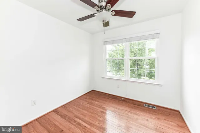an empty room with wooden floor ceiling fan and windows
