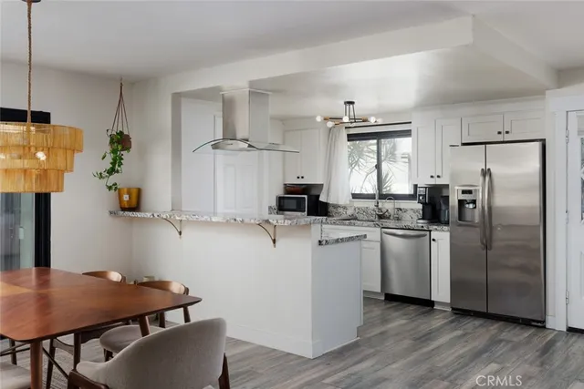 a kitchen with stainless steel appliances granite countertop a refrigerator a sink dishwasher a stove a dining table and chairs with wooden floor