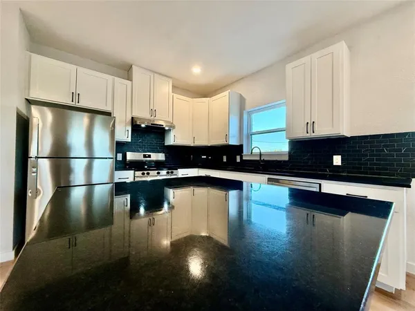 a kitchen with stainless steel appliances a refrigerator a stove a sink cabinets and a wooden floor