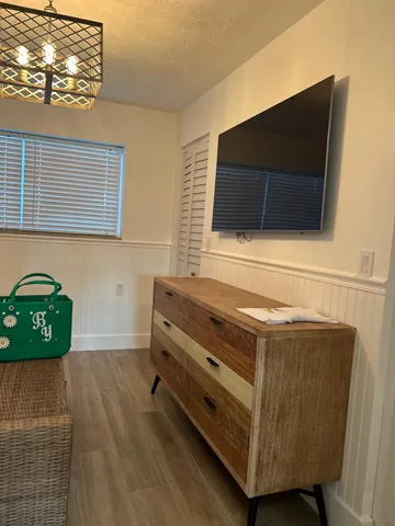 a living room with a flat screen tv on dresser and a wooden floor