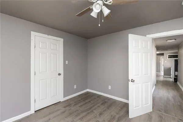 an empty room that has a chandelier fan and wooden floor