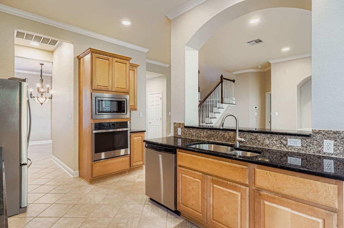 5000 Mission Oaks Boulevard, Unit 61 Austin, TX 78735 - Photo 8 of 27 Kitchen featuring crown molding, stainless steel appliances, dark stone countertops, light tile patterned flooring, and a chandelier