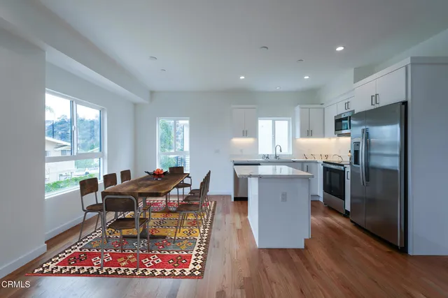 a kitchen with stainless steel appliances granite countertop a refrigerator oven a stove top oven a dining table and chairs with wooden floor