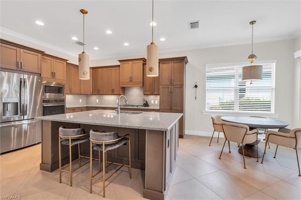 5769 Anegada Drive Naples, FL 34113 - Photo 10 of 45 a kitchen with kitchen island a dining table chairs wooden cabinets and refrigerator