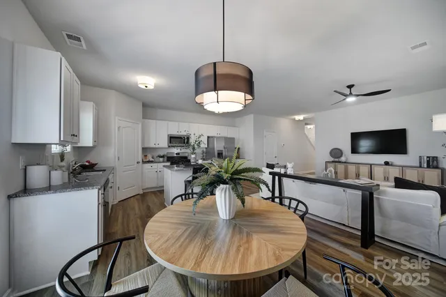 a kitchen with stainless steel appliances granite countertop a sink a stove a dining table and chairs with wooden floor