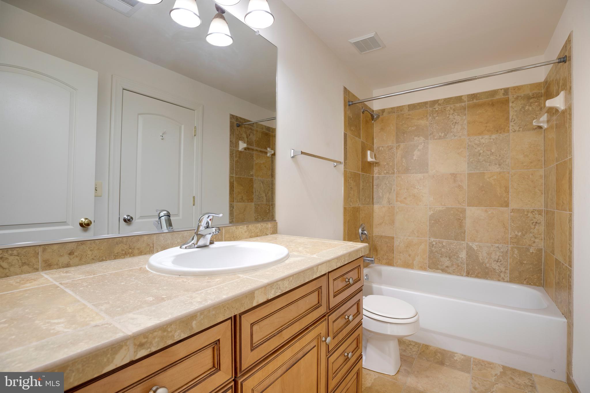 8277 Roxborough Loop Gainesville, VA 20155 - Photo 60 of 85 a bathroom with a granite countertop sink a toilet a mirror and bathtub