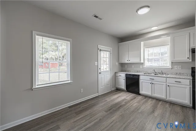 a large kitchen with granite countertop a stove top oven a sink dishwasher and white cabinets with wooden floor