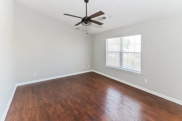 an empty room with wooden floor fan and windows