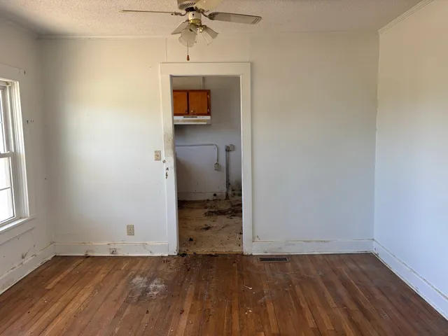 an empty room with wooden floor a ceiling fan and windows