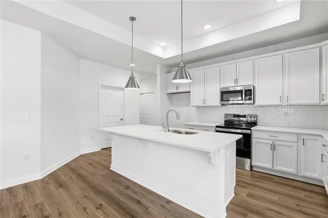 a kitchen with stainless steel appliances granite countertop a sink a stove a refrigerator and white cabinets with wooden floor