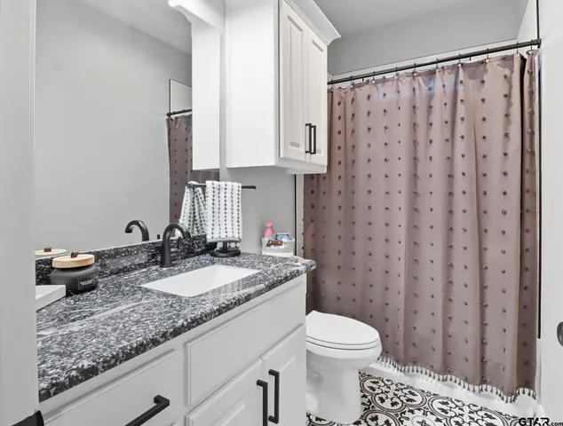 a bathroom with a granite countertop sink a toilet a mirror and shower curtain