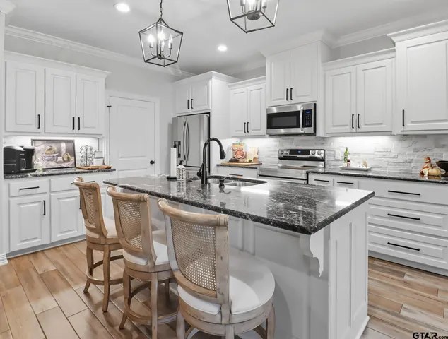 a kitchen with stainless steel appliances granite countertop a sink a stove a refrigerator cabinets and chairs