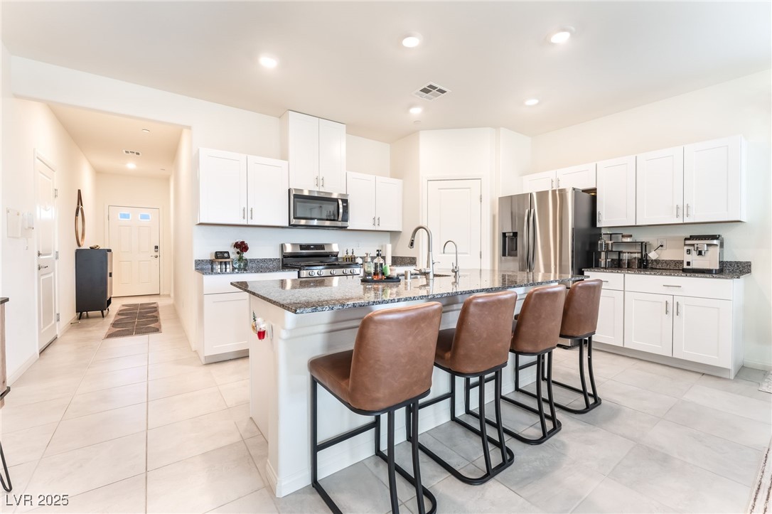 10947 Artisan Ranch Avenue Las Vegas, NV 89166 - Photo 12 of 39 Kitchen featuring white cabinetry, dark stone counters, a kitchen bar, appliances with stainless steel finishes, and a kitchen island with sink