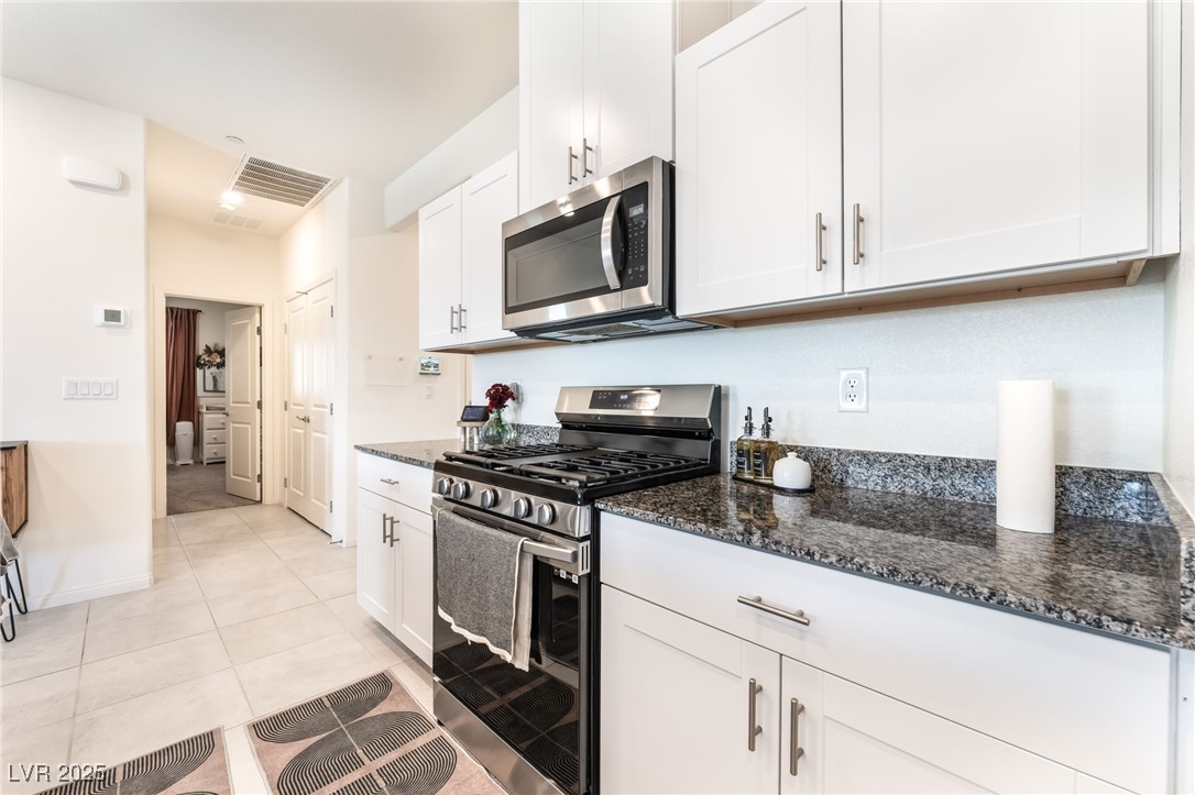 10947 Artisan Ranch Avenue Las Vegas, NV 89166 - Photo 14 of 39 Kitchen featuring appliances with stainless steel finishes, dark stone counters, white cabinets, and light tile patterned floors