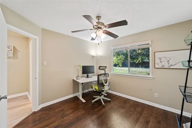 a view of an empty room with wooden floor and a fan