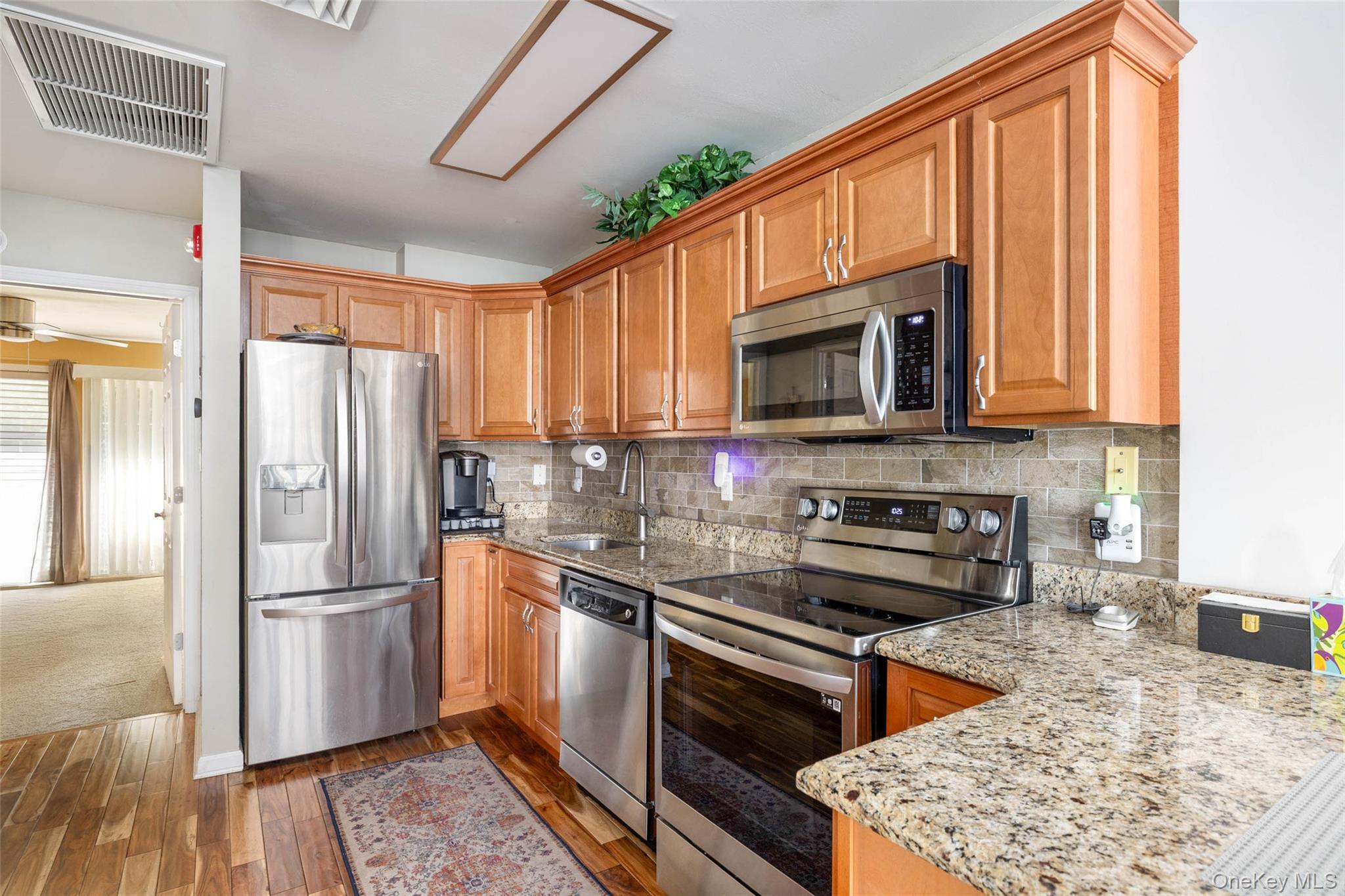 121 Willow Lane Valley Stream, NY 11580 - Photo 10 of 30 Kitchen with appliances with stainless steel finishes, light stone countertops, dark wood-style floors, decorative backsplash, and brown cabinetry