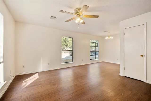 an empty room with wooden floor chandelier fan and windows