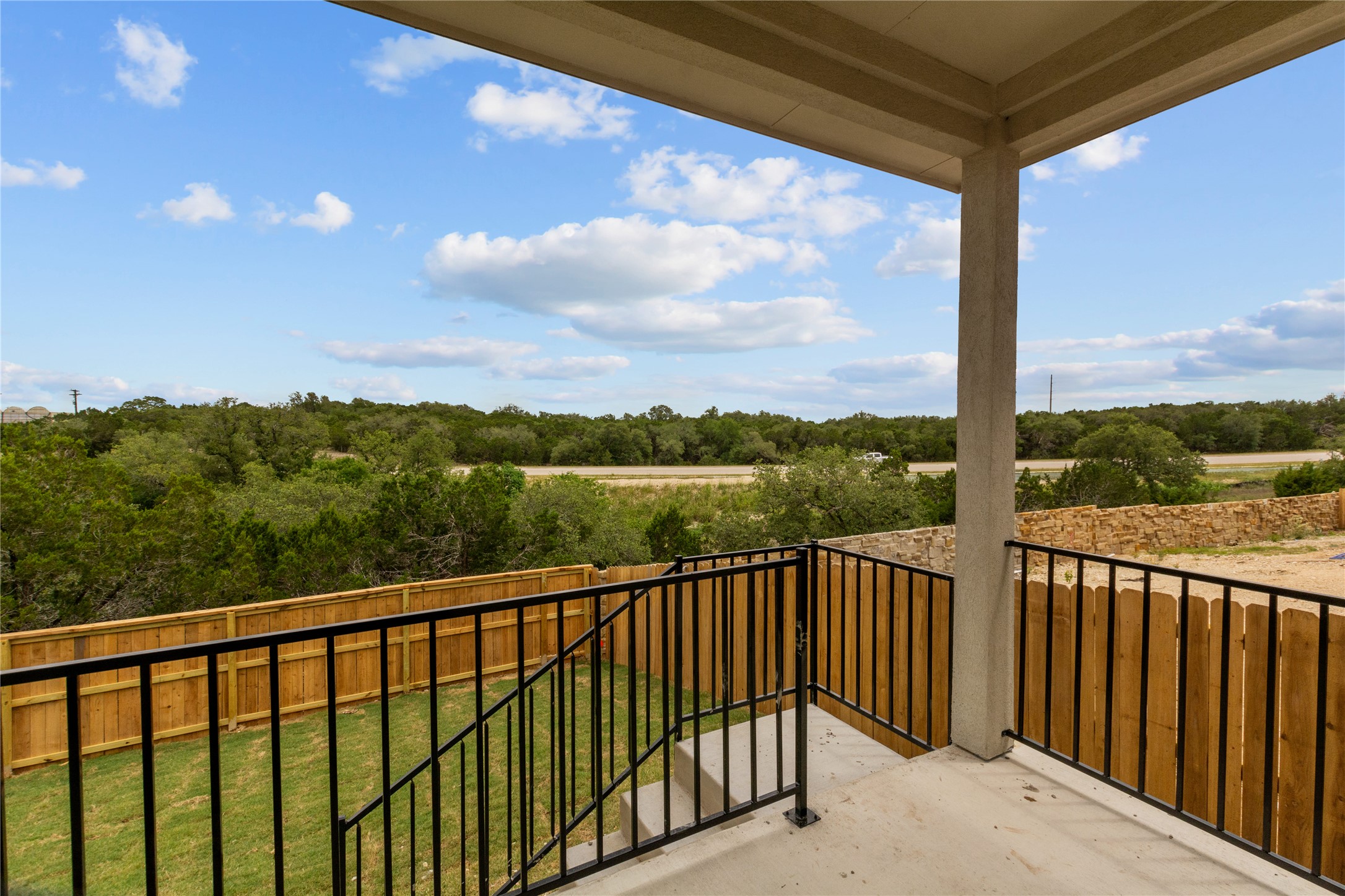 1108 Mallow Road Leander, TX 78641 - Photo 22 of 30 An elevated covered patio looks out over a fenced yard toward distant trees and rolling hills.