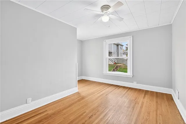 an empty room with wooden floor chandelier fan and windows