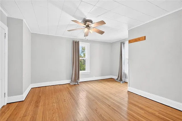 an empty room with wooden floor chandelier fan and windows