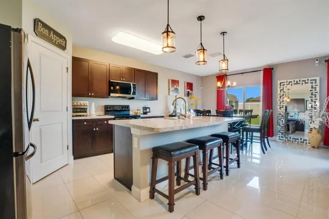 a kitchen with stainless steel appliances granite countertop a refrigerator a stove a sink a dining table and chairs with wooden floor