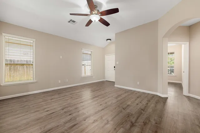 an empty room with wooden floor ceiling fan and windows