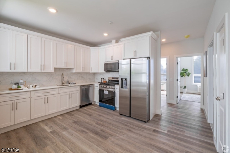 141 Crooks Avenue, Unit 501 Clifton, NJ 07011 - Photo 5 of 7 a kitchen with granite countertop a refrigerator oven a sink dishwasher and white cabinets with wooden floor