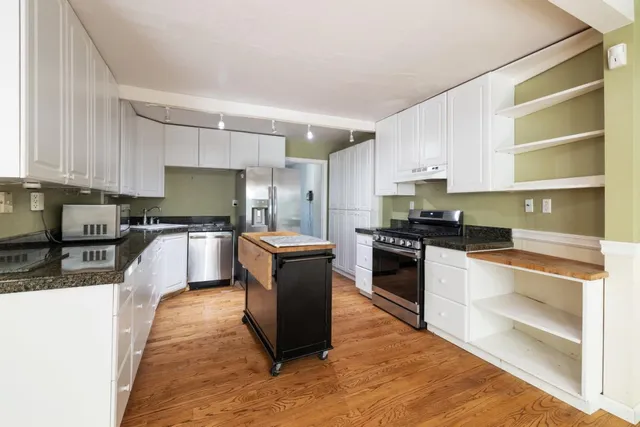 a kitchen with granite countertop a stove a sink and white cabinets with wooden floor