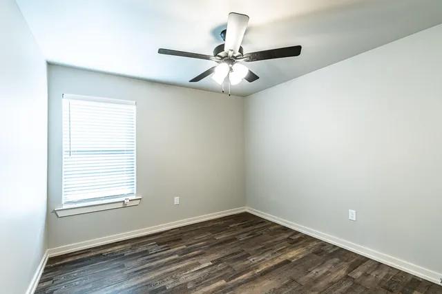 an empty room with wooden floor fan and windows