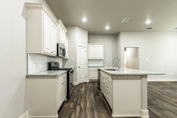 a kitchen with stainless steel appliances granite countertop a stove a sink a refrigerator and white cabinets with wooden floor