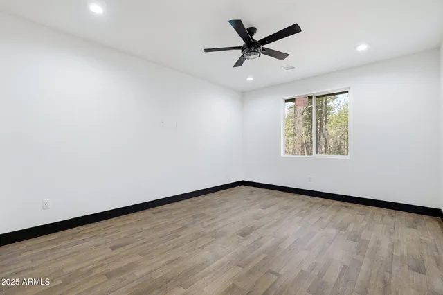 an empty room with wooden floor ceiling fan and windows