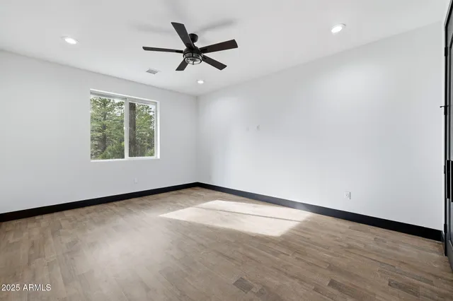 an empty room with wooden floor fan and windows