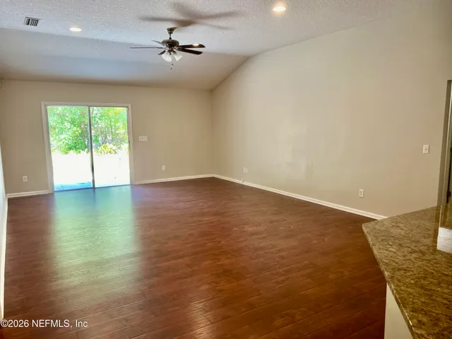 an empty room with wooden floor chandelier fan and windows