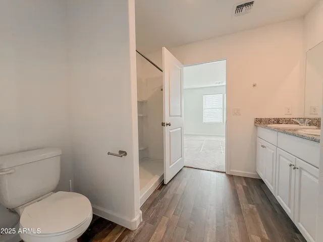 a bathroom with a granite countertop toilet a sink and wooden floor