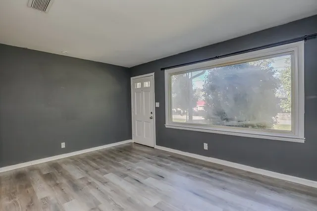a view of an empty room with wooden floor and a window