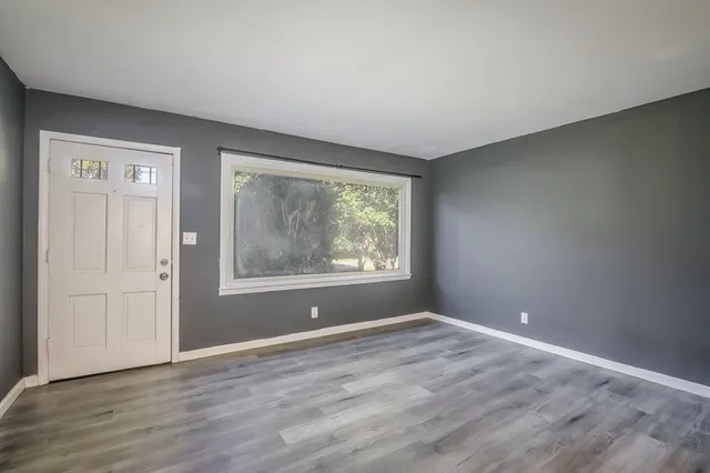 a view of an empty room with wooden floor and a window