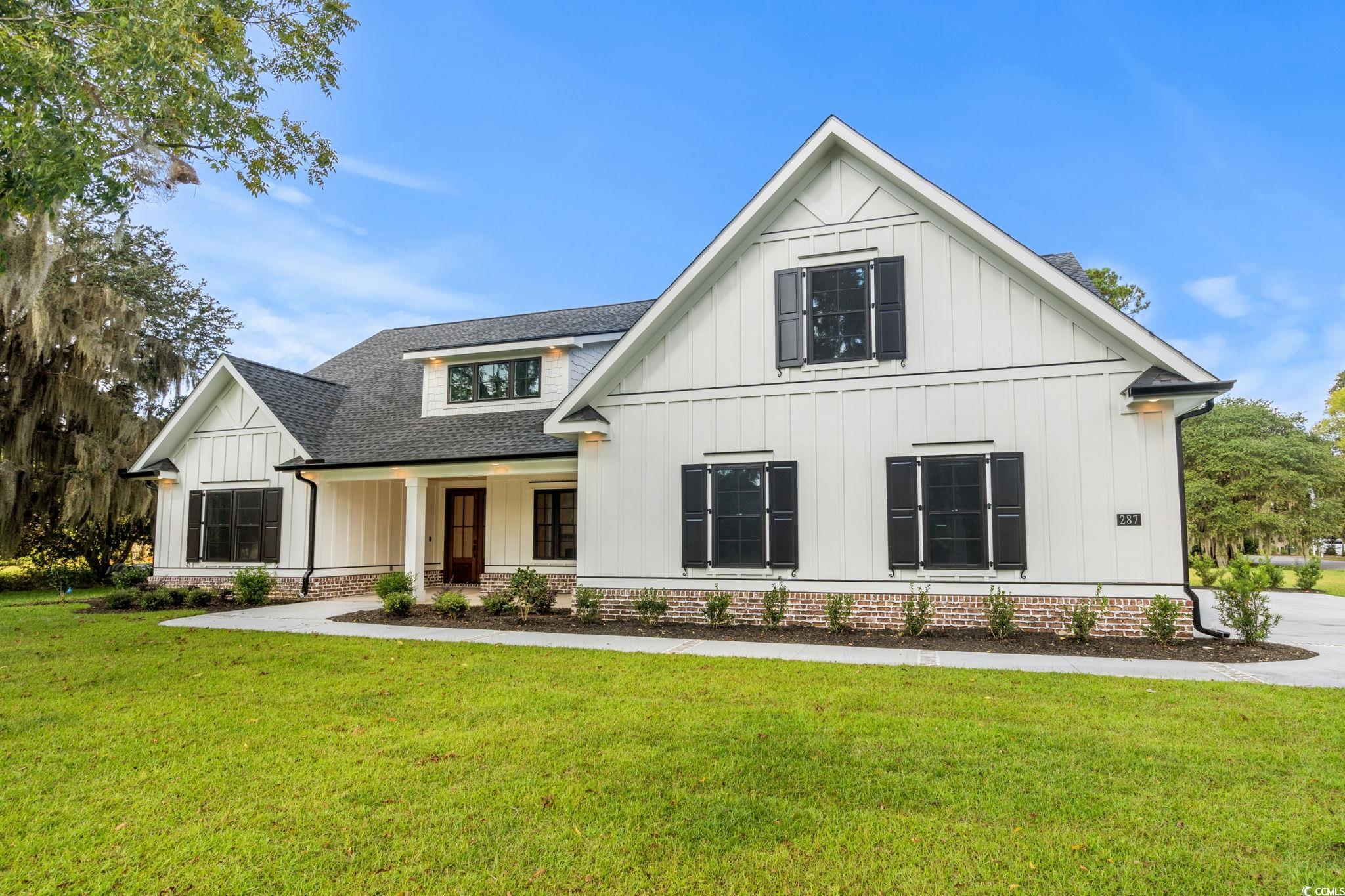 Modern farmhouse style home with board and batten siding, covered porch, a front lawn, and a shingled roof