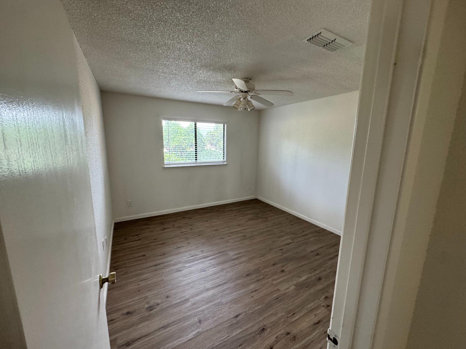 21293 East American Avenue Reedley, CA 93654 - Photo 8 of 19 an empty room with wooden floor ceiling fan and windows