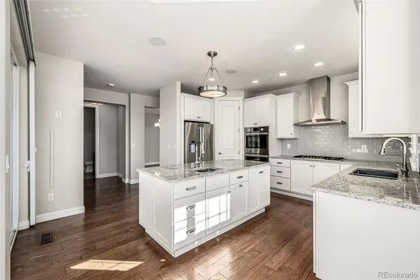 a large kitchen with granite countertop a stove top oven a sink a refrigerator and white cabinets with wooden floor