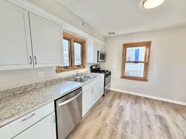 a large kitchen with granite countertop a stove a sink and a dishwasher with wooden floor