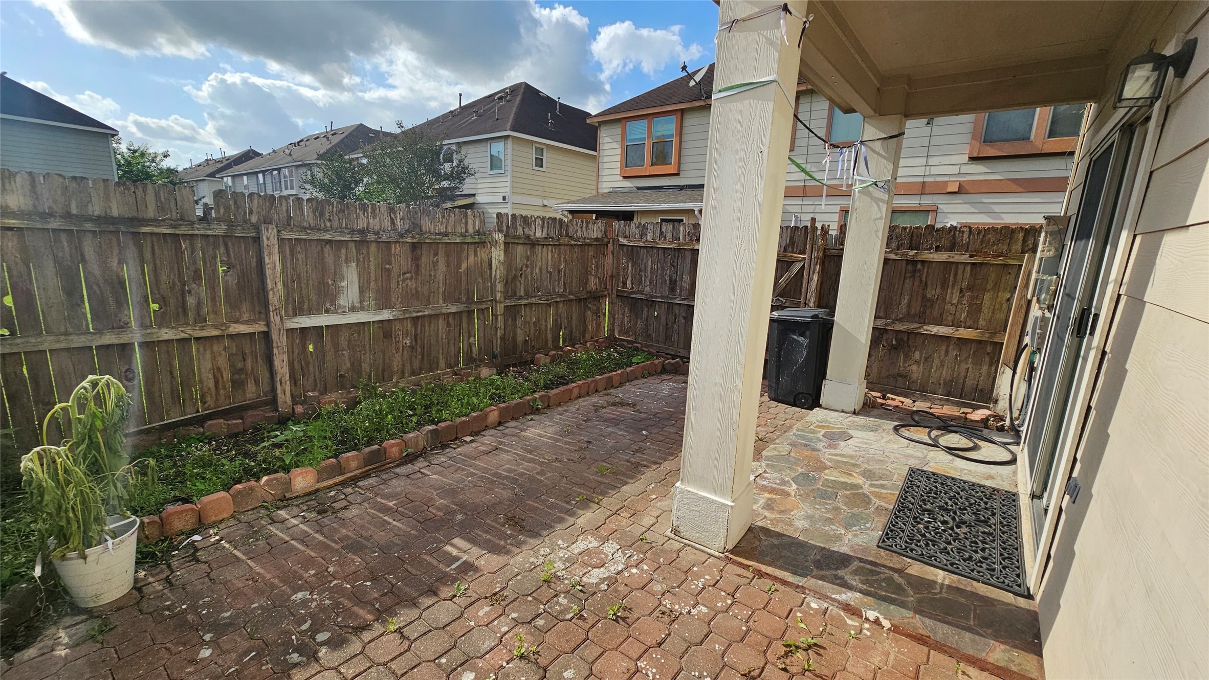 7918 Barnes Ridge Lane Houston, TX 77072 - Photo 30 of 34 This photo shows a fenced backyard with a paved patio area. It features a wooden fence, a potted plant, and a covered section near the house, offering a cozy outdoor space for relaxation or small gatherings.