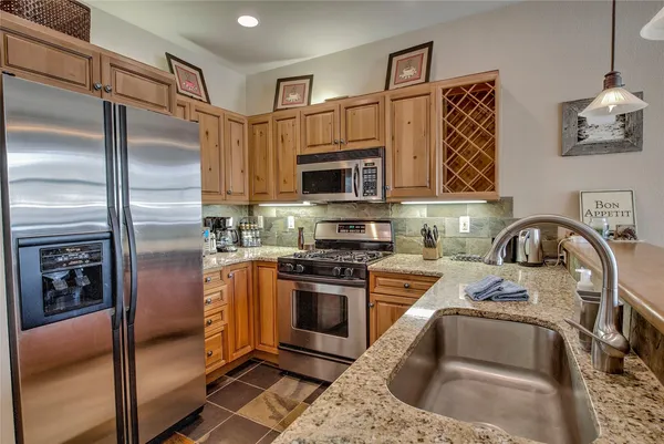 a kitchen with stainless steel appliances granite countertop a refrigerator a stove and a sink with wooden floor